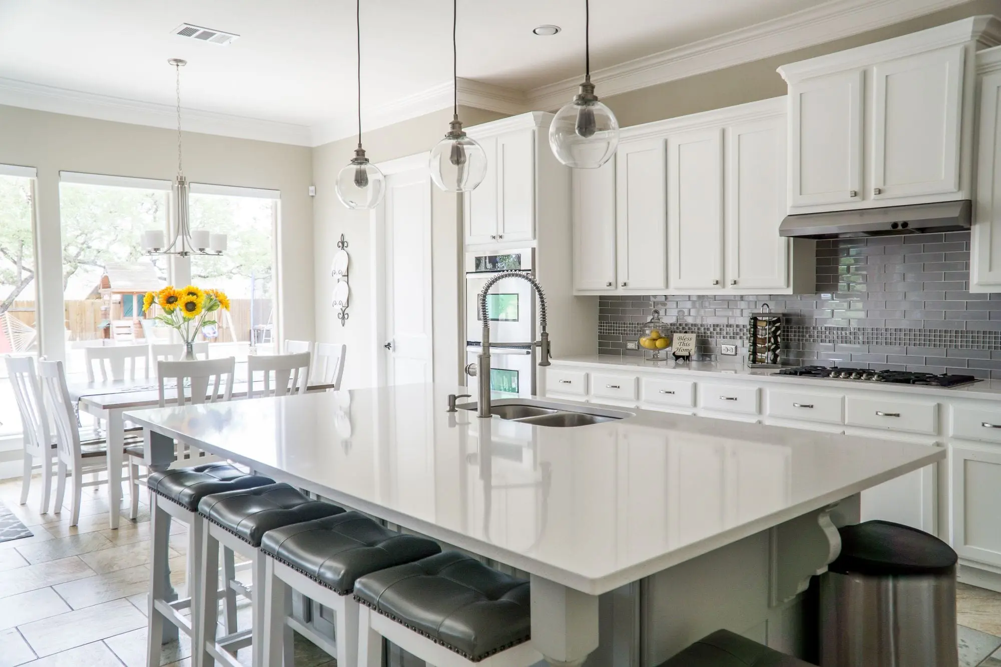 A bright white home kitchen with a large island, bar stools and pendant lights