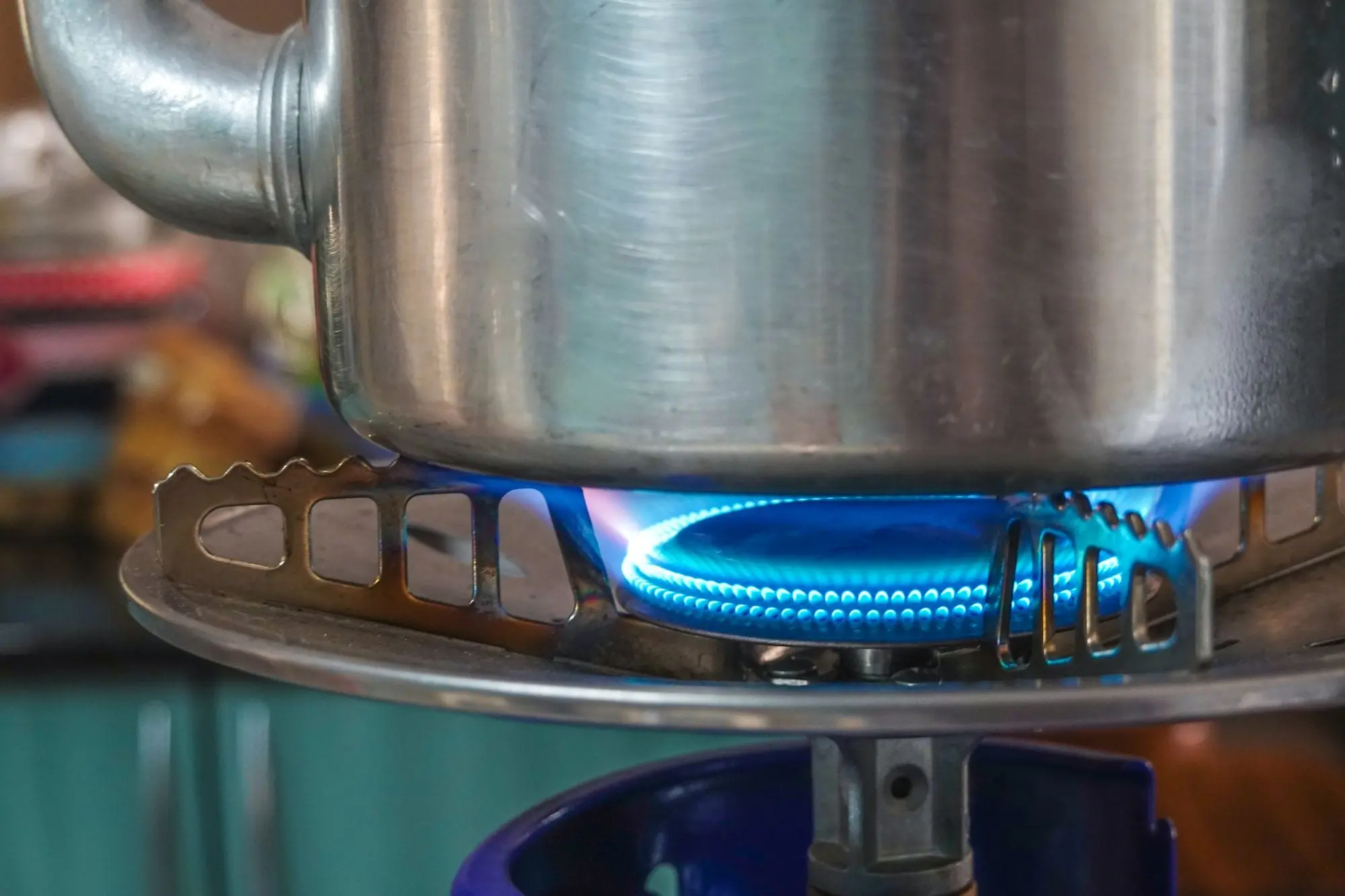 A stainless steel kettle heating over a blue gas flame