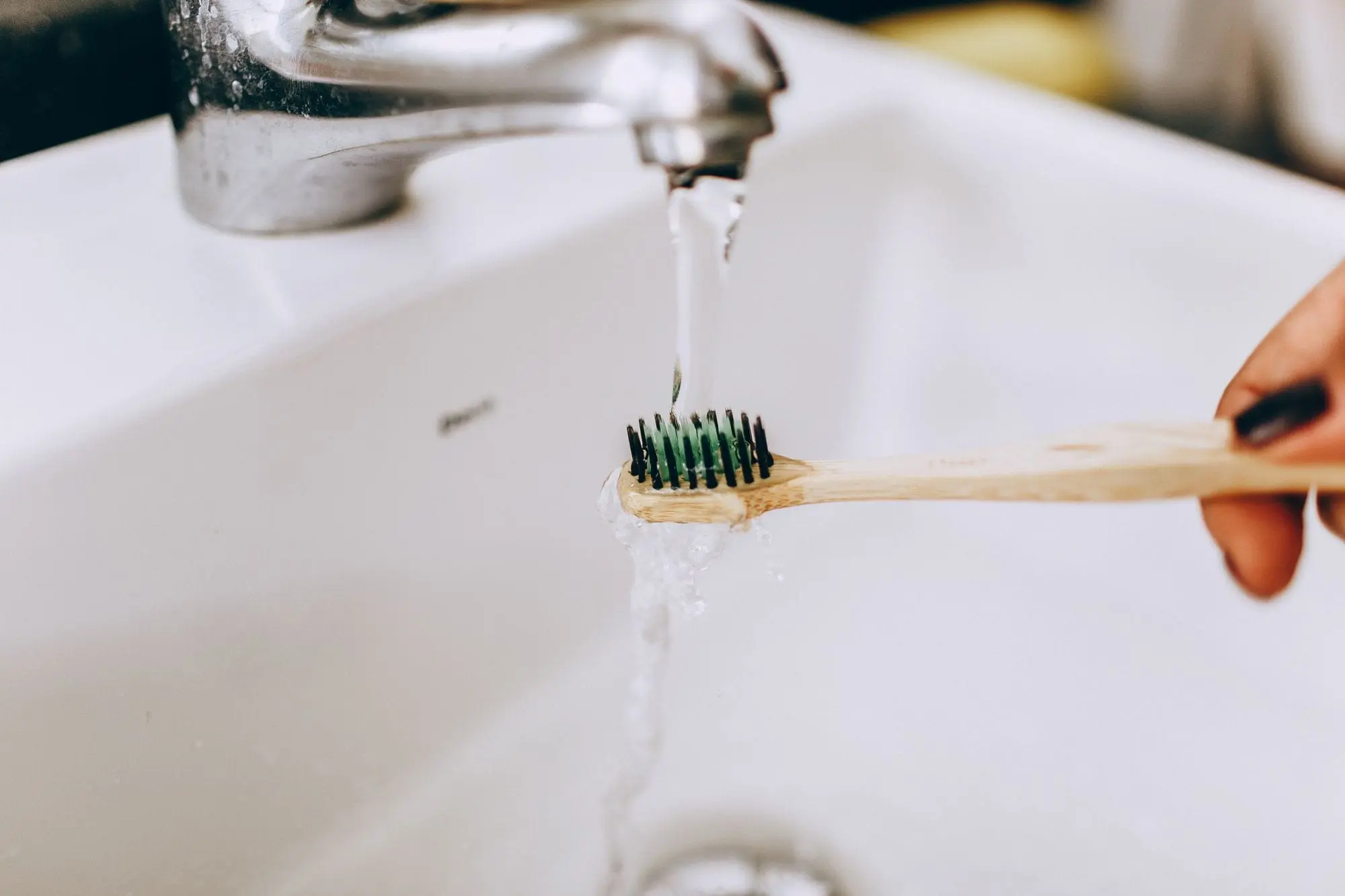 A bamboo toothbrush held under a running bathroom tap