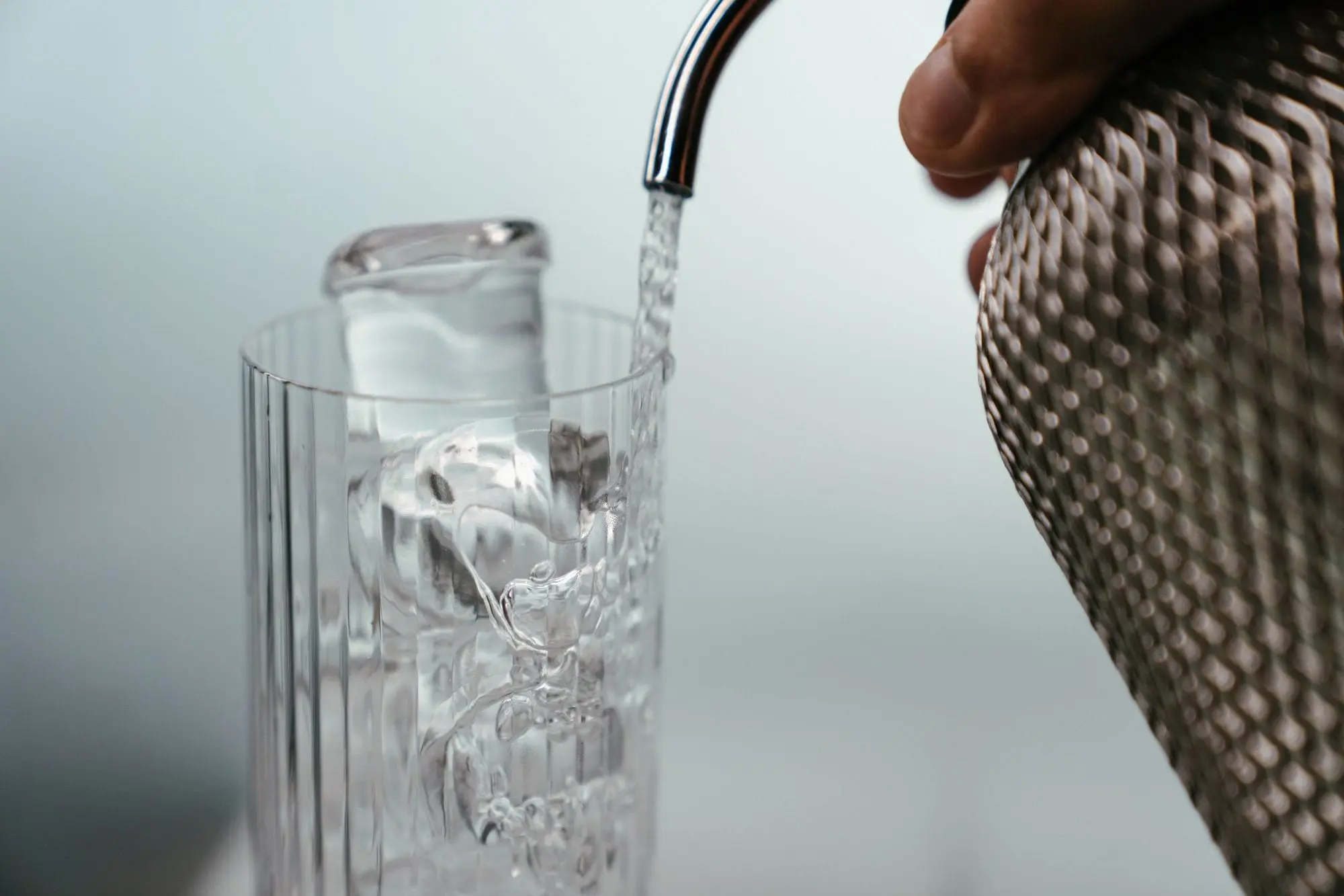 Sparkling water being poured into a tall glass with ice cubes