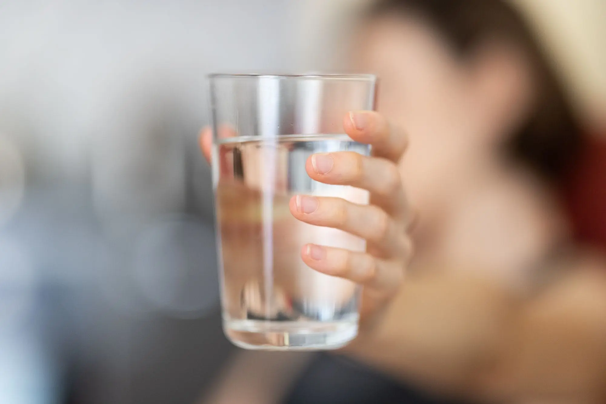 Hand holding a glass of clear water, blurred background