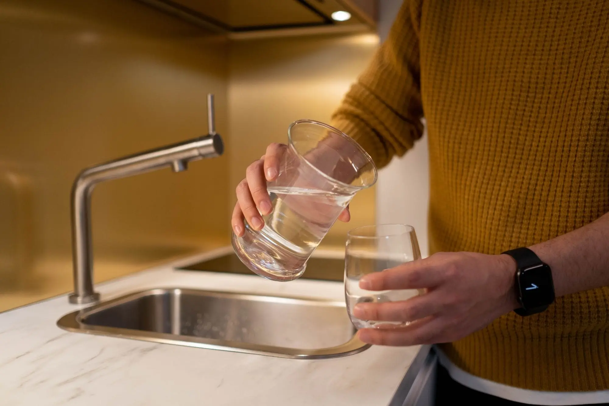 Person pouring water from a jug into a glass at a kitchen sink