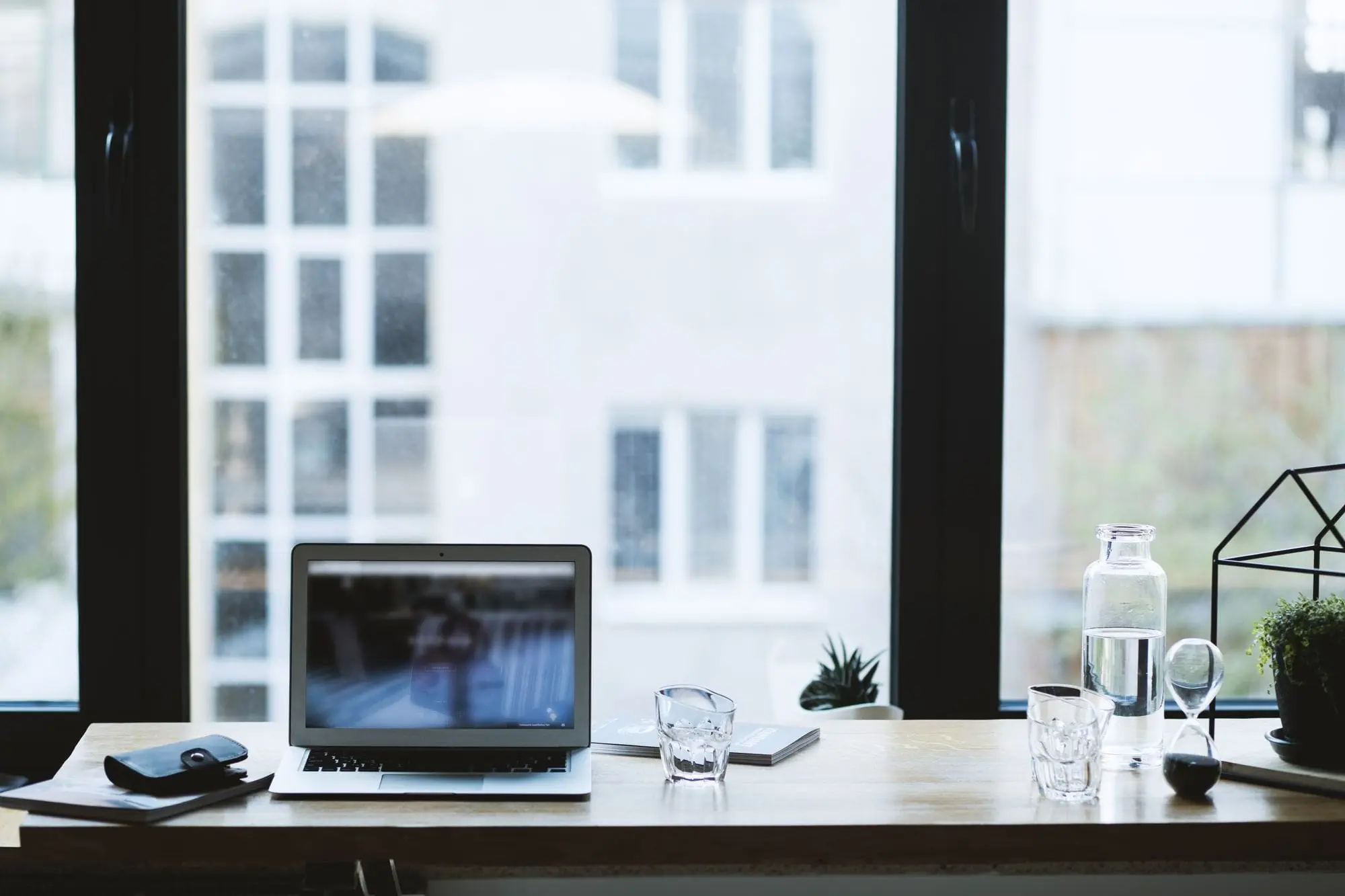 Laptop and a glass of water on a desk by a window
