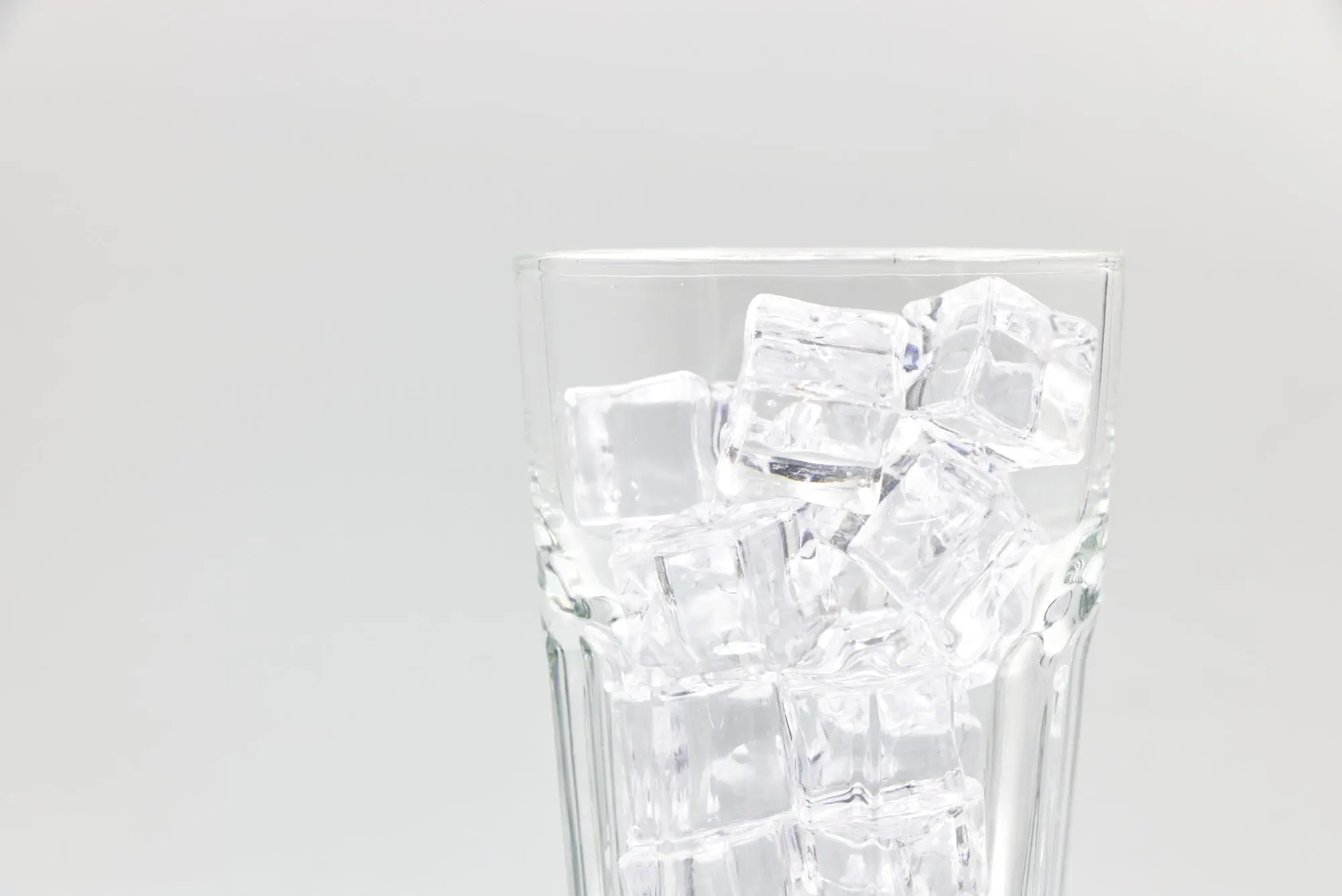 A clear glass filled with ice cubes on a white background