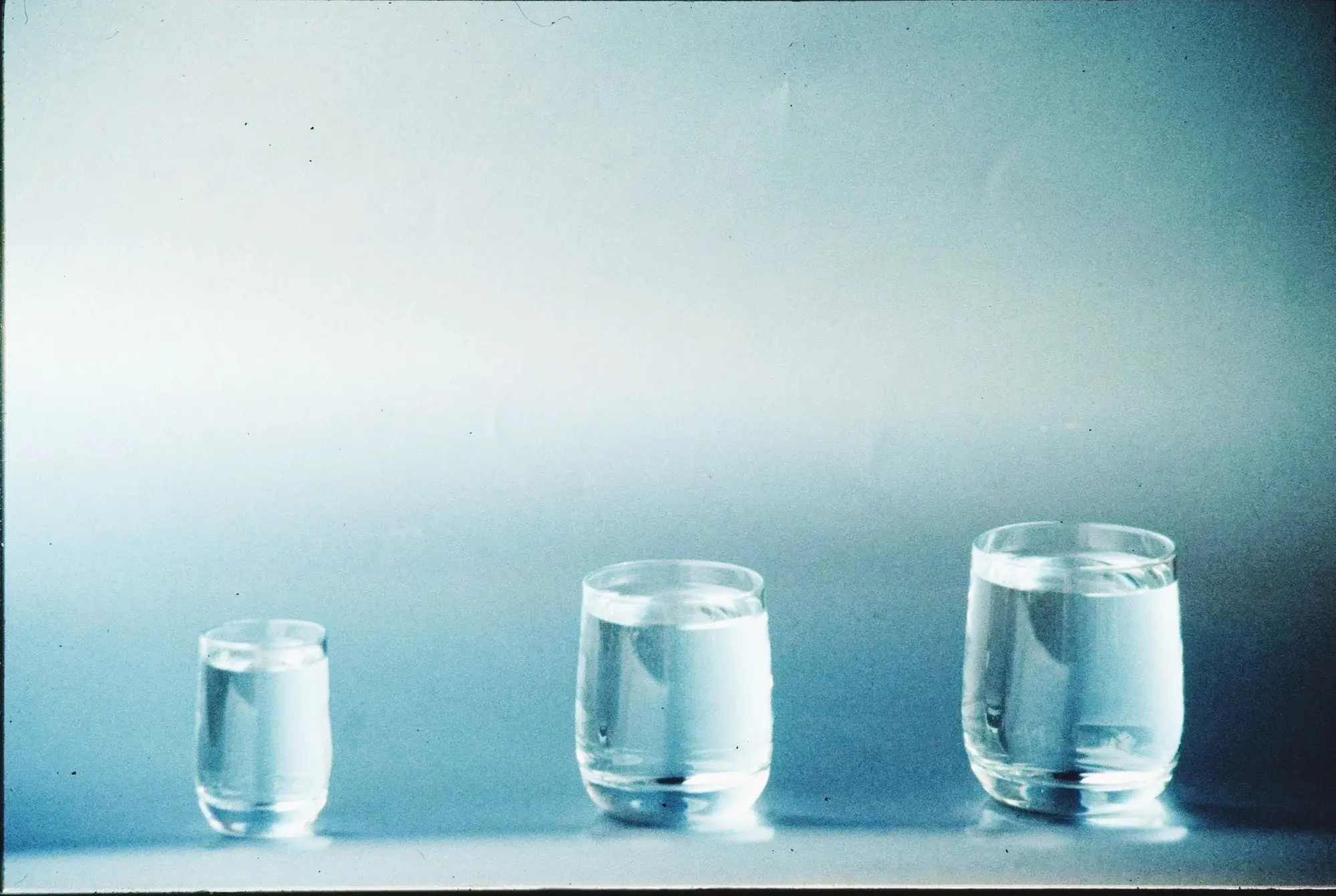 Three glasses of water of different sizes on a blue background