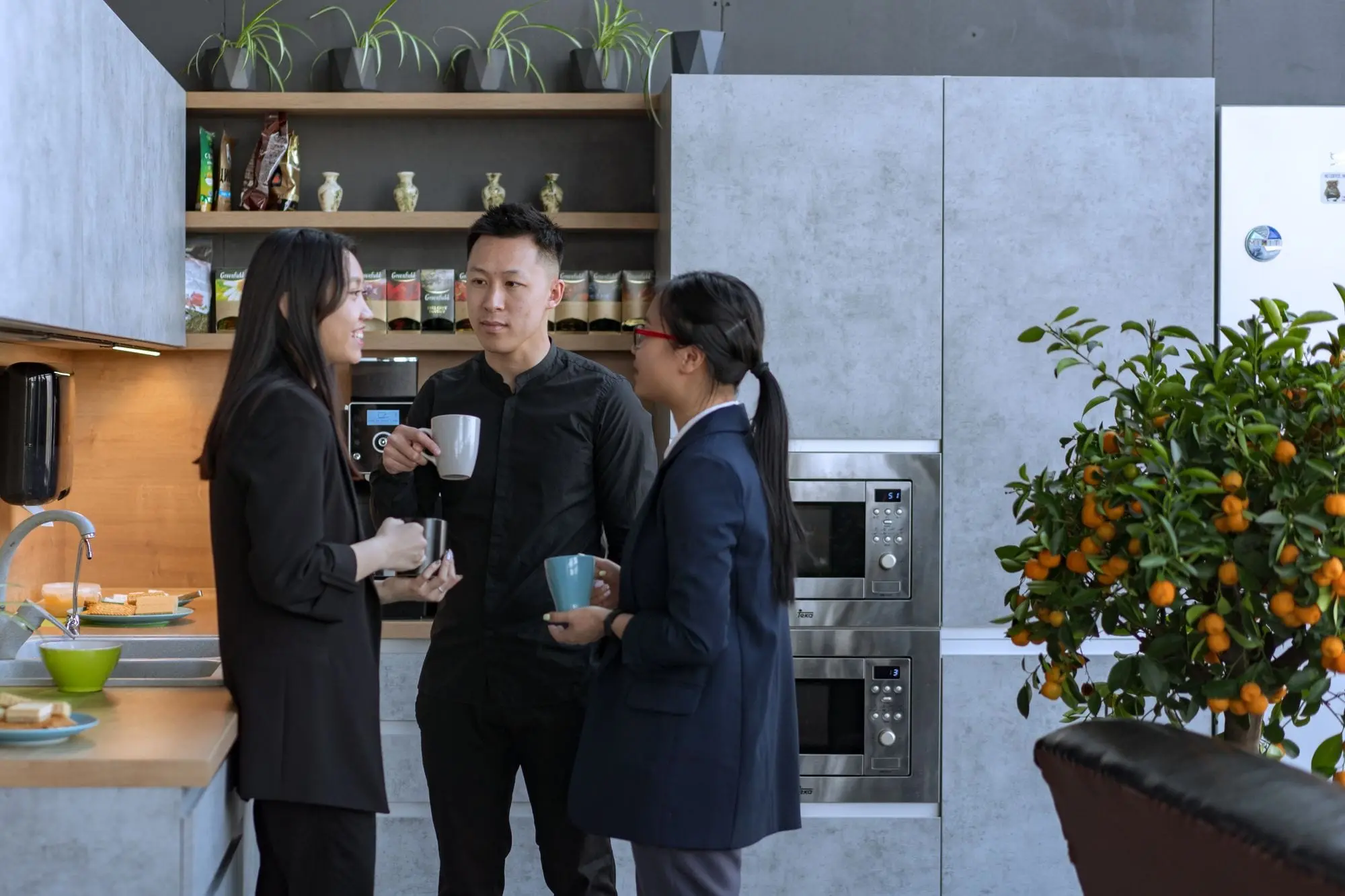 Three colleagues holding mugs during a break in a modern office kitchen