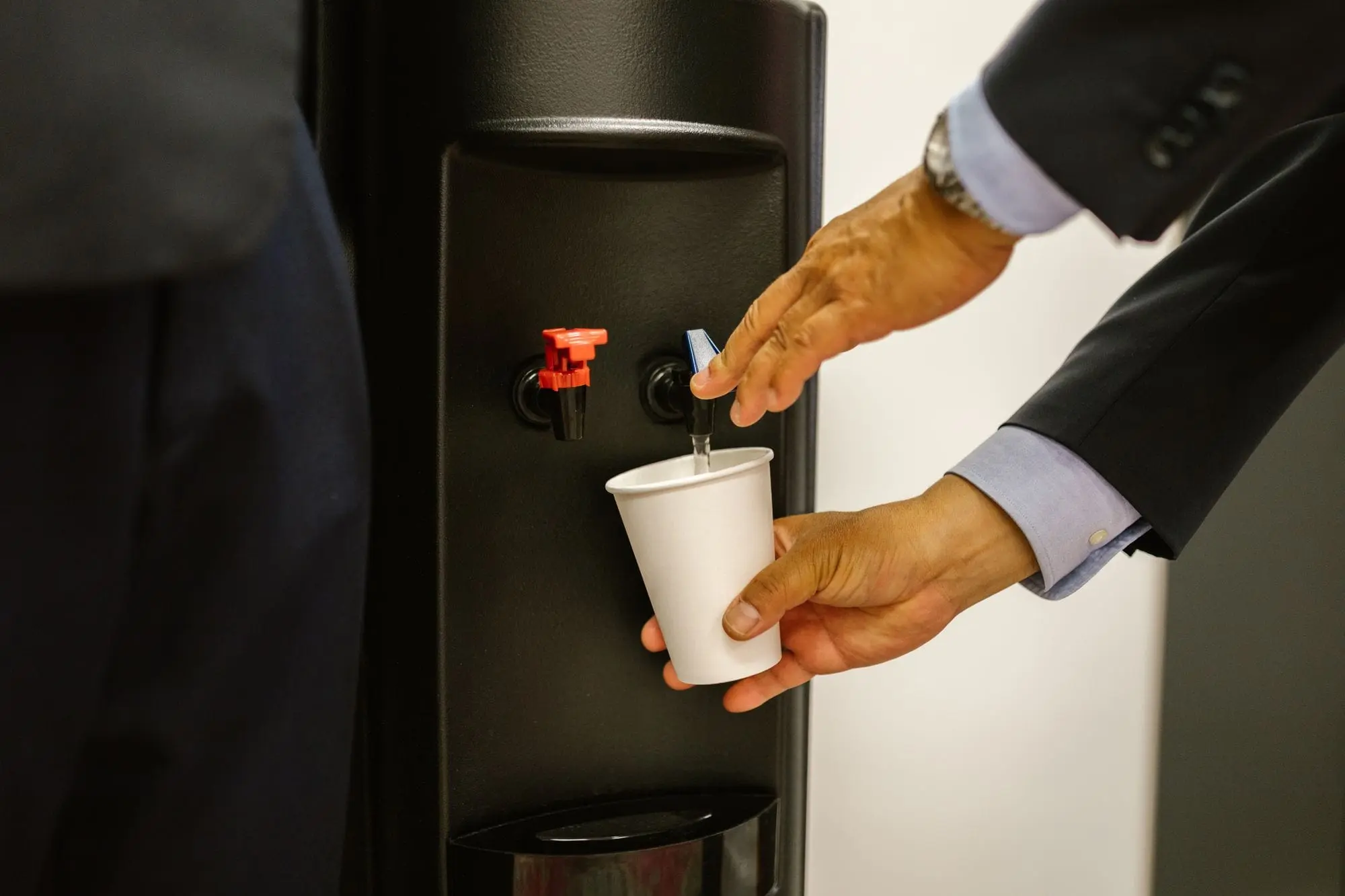 Man in a suit filling a paper cup at an office water dispenser
