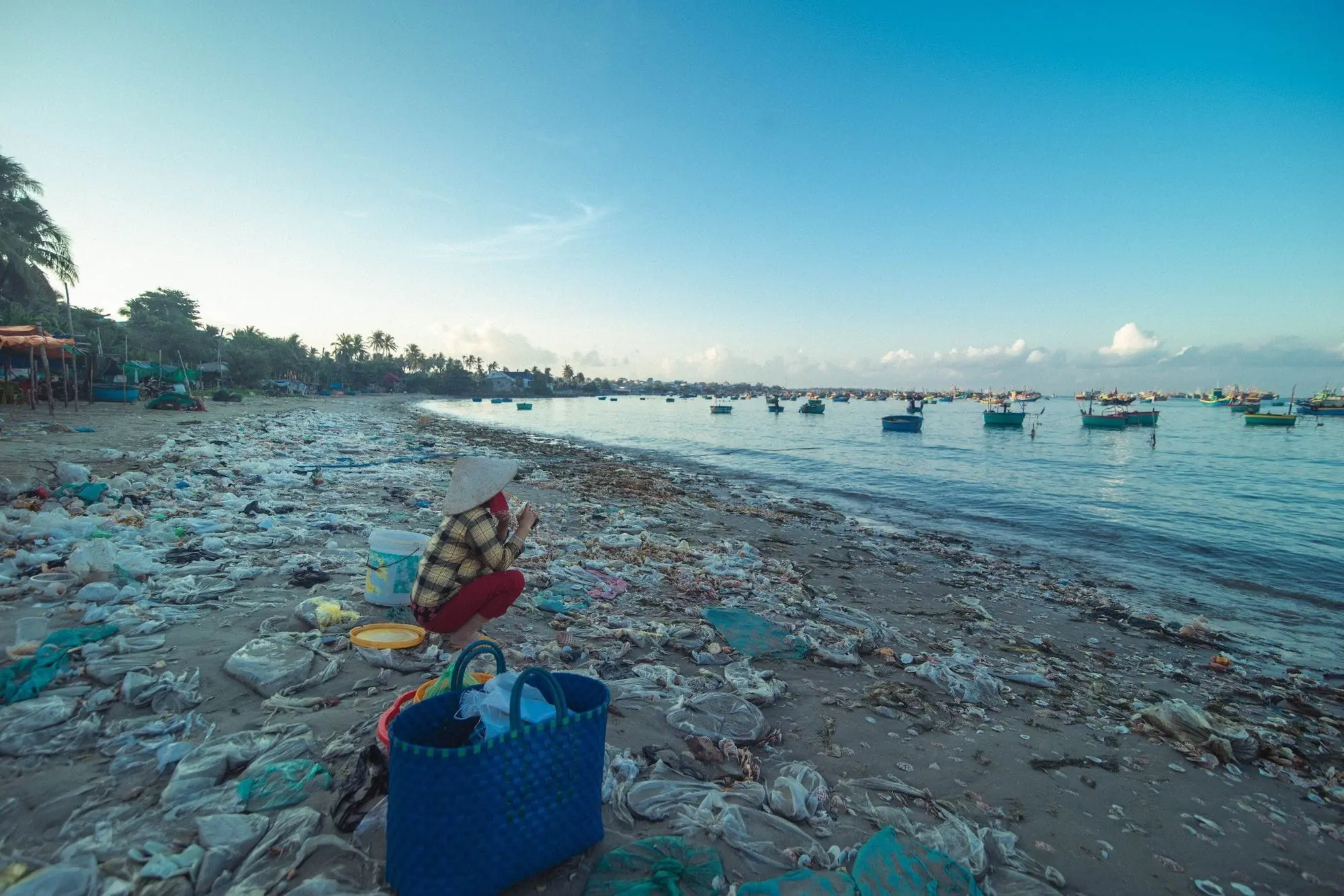 Beach covered in plastic waste with fishing boats offshore