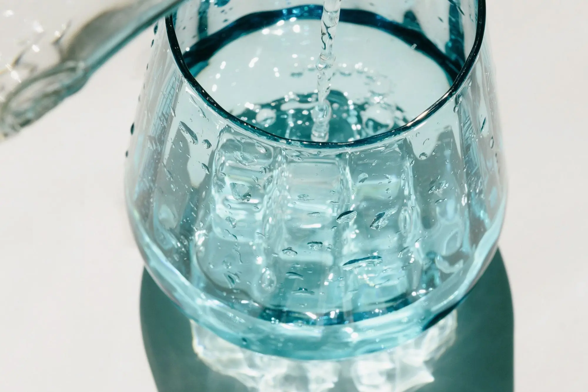 Water poured from a glass bottle into a drinking glass, seen from above