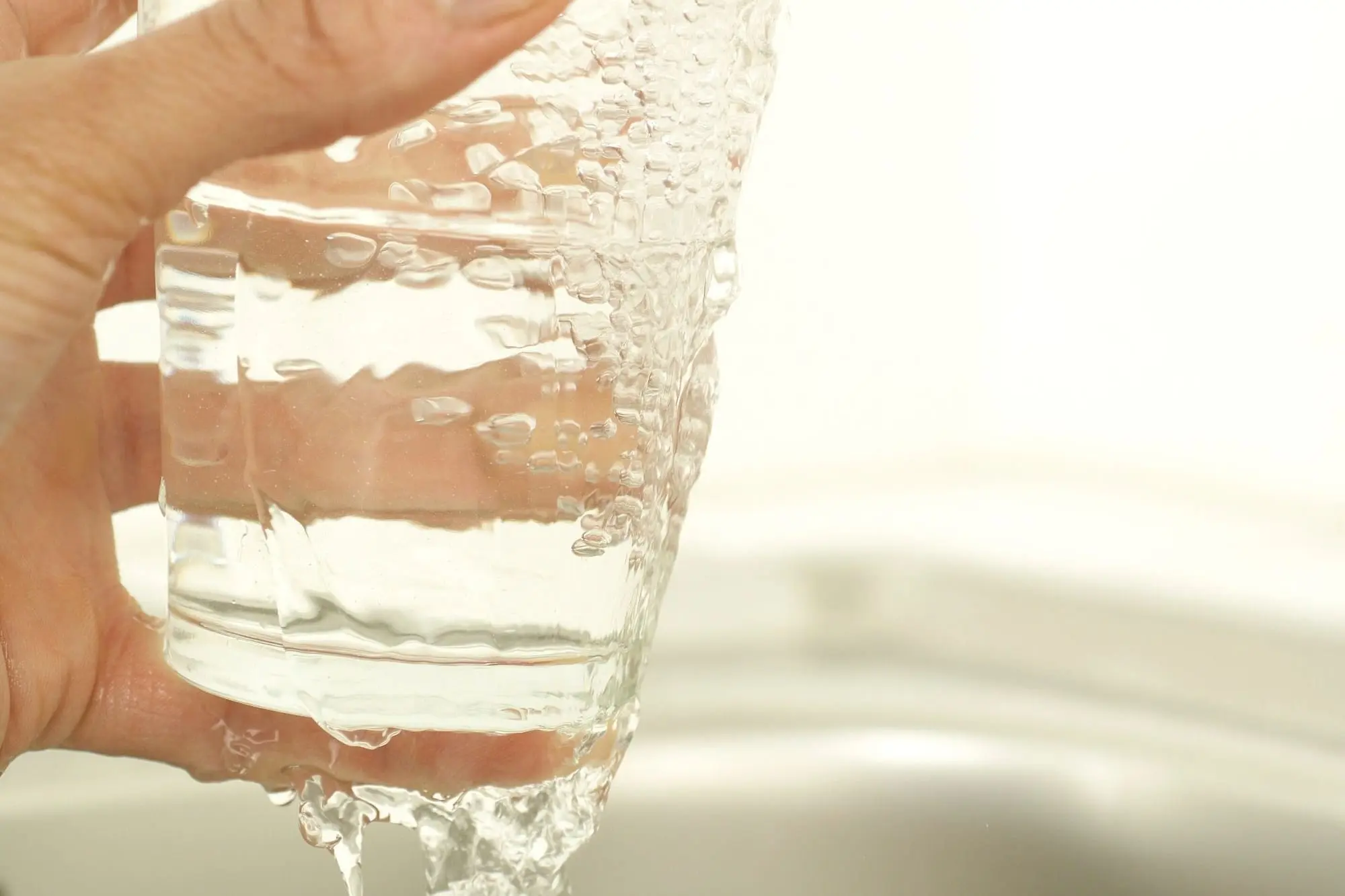 A hand holding a glass as it fills with water from a tap