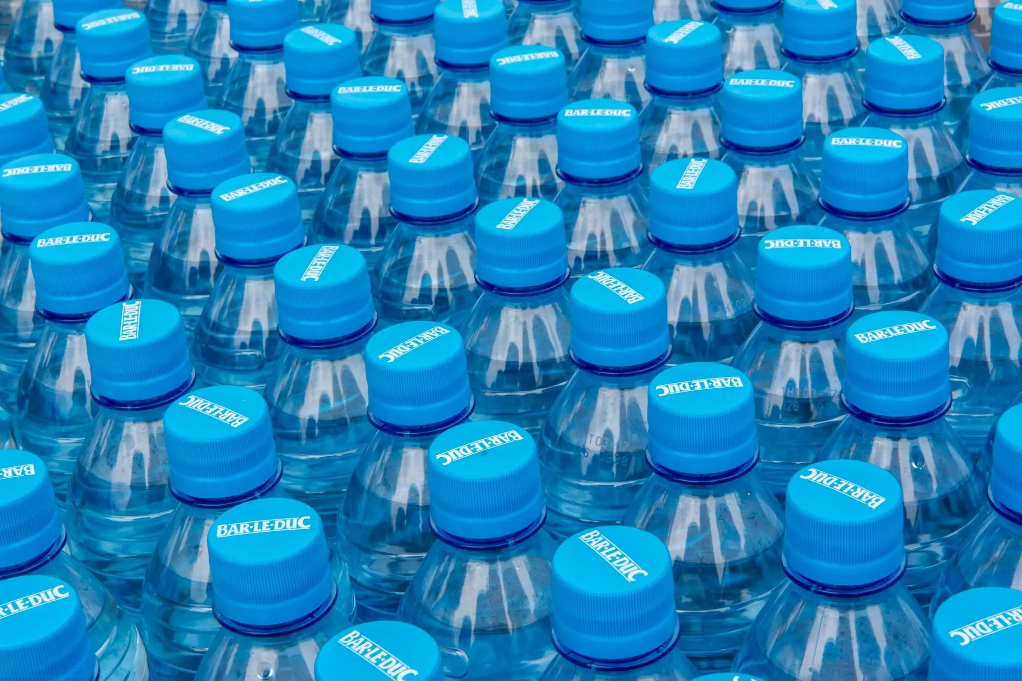 Rows of plastic water bottles with blue caps stacked in a shop