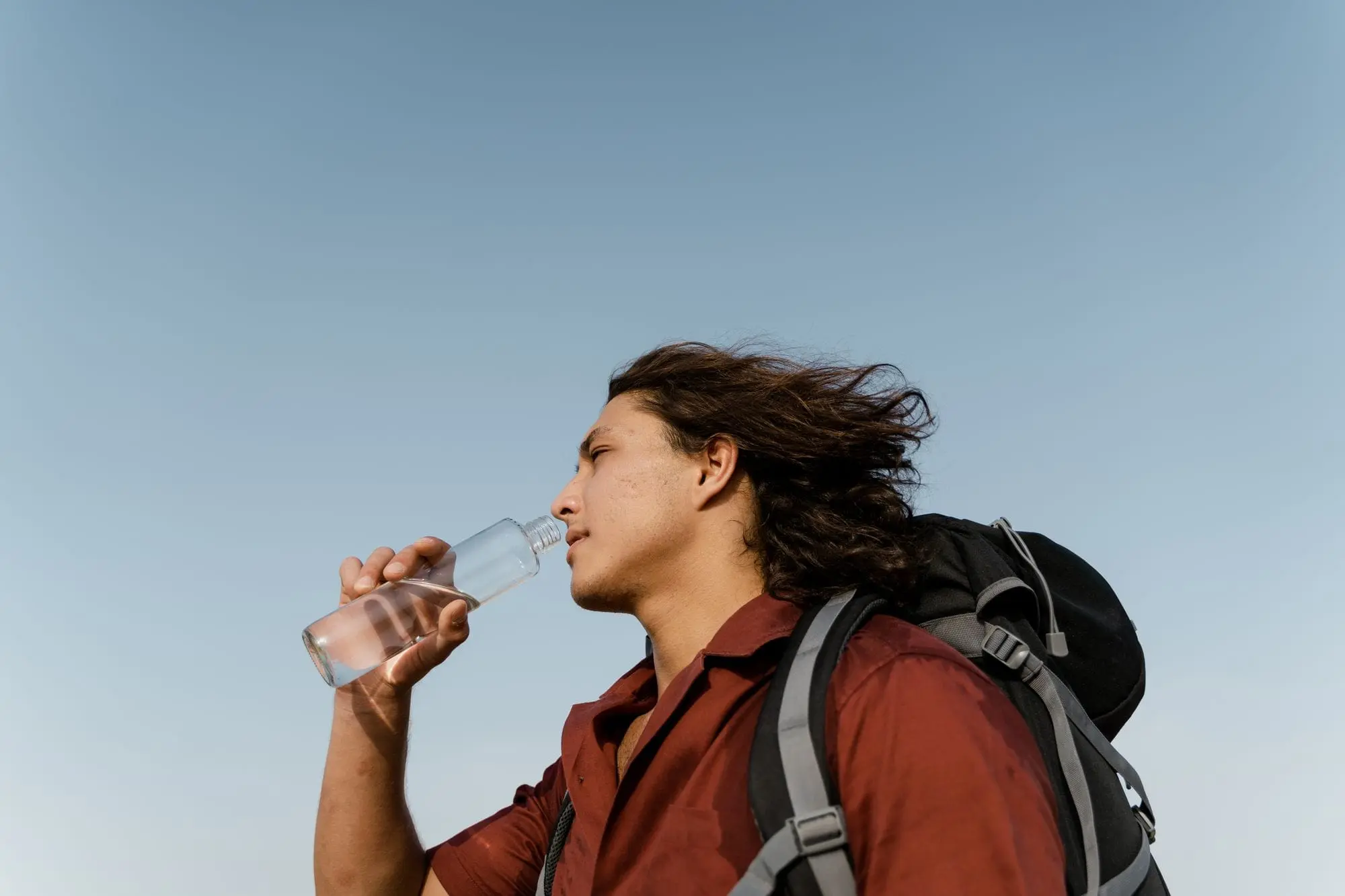 Hiker with a backpack drinking water from a glass bottle