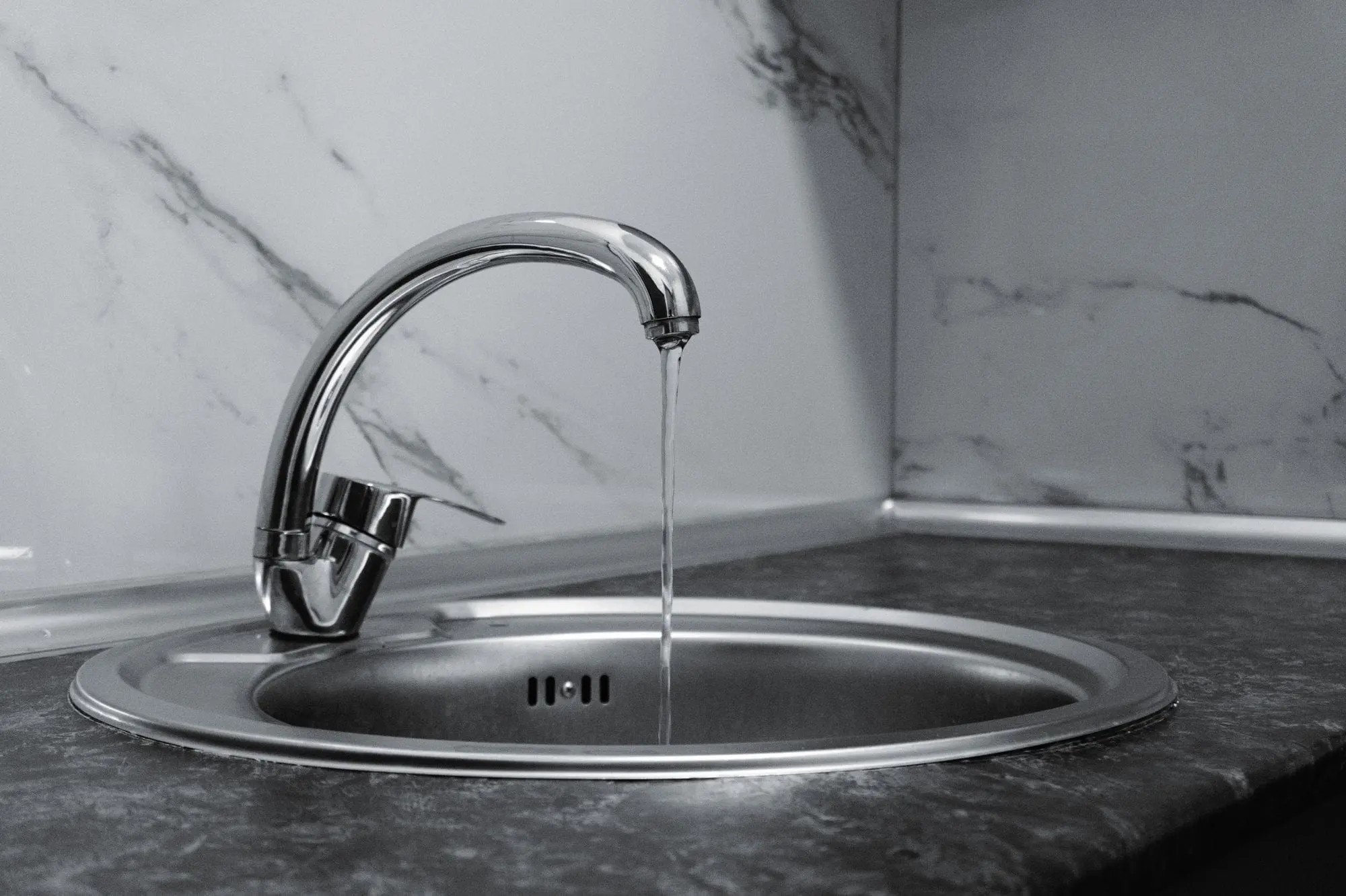 Chrome kitchen faucet with running water over a steel sink