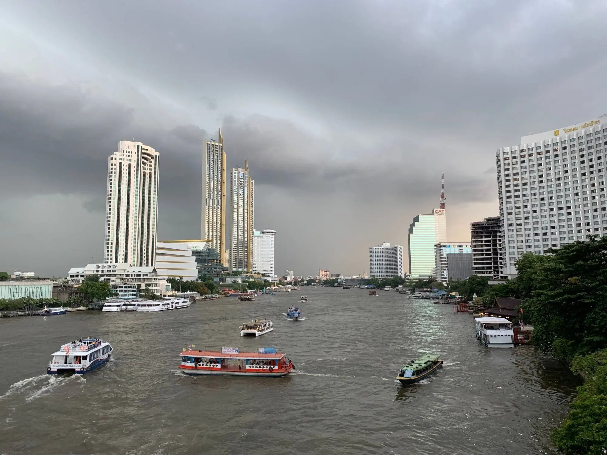 Boats on the Chao Phraya River with Bangkok skyscrapers under a stormy sky