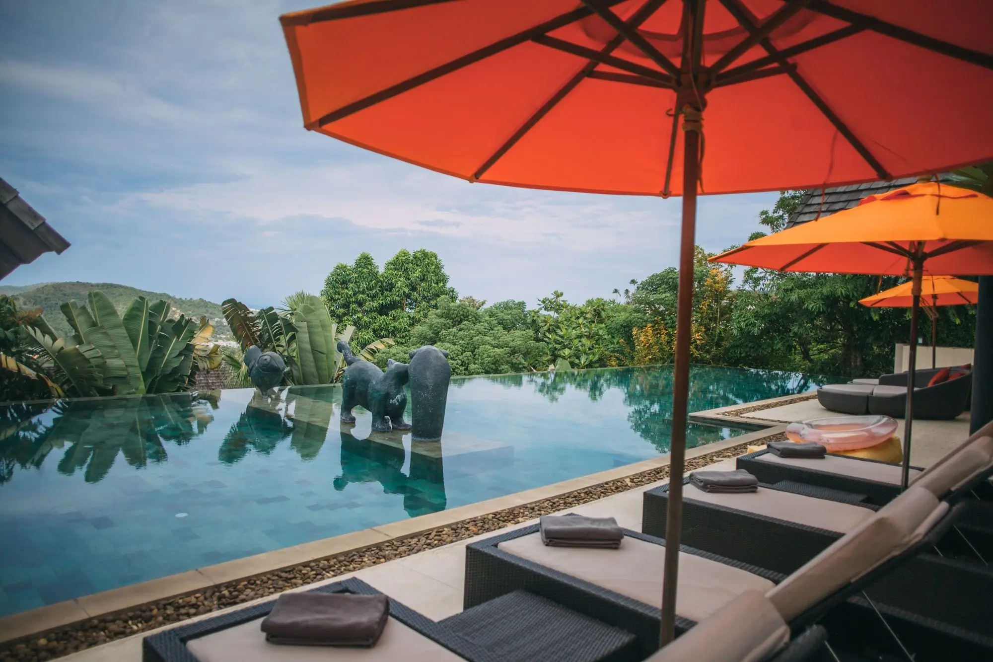 Infinity pool of a hillside villa in Koh Samui with orange parasols and sun loungers